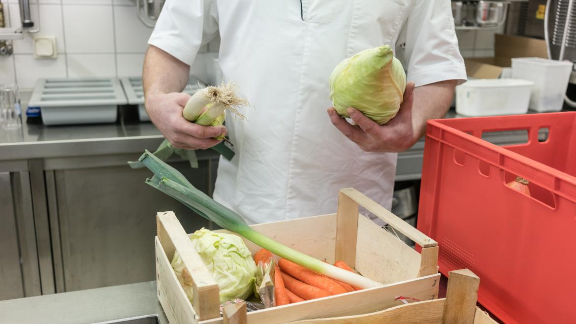 Koch hält Lauch und Spitzkohl in der Hand