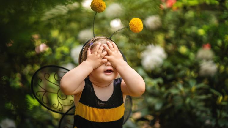 Kind im Bienenkostüm steht im Garten und hält sich die Augen zu.