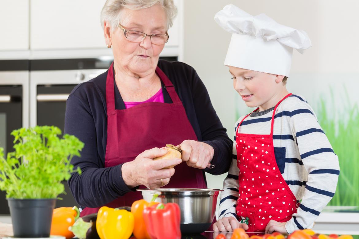 Ältere Dame mit Kind in der Küche am Kartoffeln schälen. Der Junge hat eine Kochmütze auf.